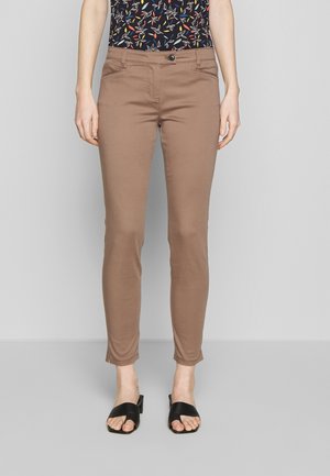 Bruine skinny broek met een gladde textuur, twee achterzakken en een enkele knoopsluiting, gecombineerd met zwarte sandalen.
