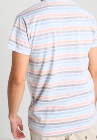 T-shirt rayé avec des lignes horizontales bleues, pêche et grises. Manches courtes et encolure ronde, fabriqué en tissu doux et léger.