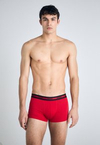 Røde boxershorts laget av bomull med svart elastisk livband som har "HUGO"-logo. Glatt tekstur, tettsittende design og midt-lår snitt.