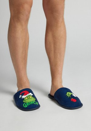Navy blue plush slippers with Grinch and holiday accents. Soft fabric with embroidered details, open back design, and textured soles.
