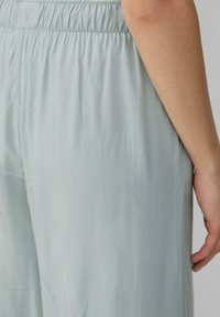 Helleblaue, weite Hosen mit elastischem Bund aus einem glatten, leichten Material, die eine Seitenansicht mit minimalem Design zeigen.