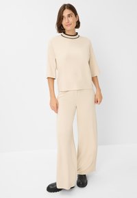Top beige con maniche corte e scollatura rifinita in nero, abbinato a pantaloni beige a gamba larga. Tessuto liscio e leggero con vestibilità comoda.