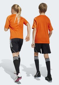 Orangefarbene Sportshirts mit kurzen Ärmeln, schwarze Shorts, schwarz-weiße Fußballsocken und Stollen mit pinken Akzenten.