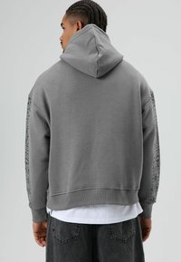 Grijze capuchontrui met een geribbelde zoom en een textuurpatroon op de mouwen. Heeft een losse pasvorm en een zachte stoftextuur.