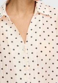 Camicia button-up rosa chiaro realizzata in un tessuto texturizzato, con pois neri e un design di colletto classico.