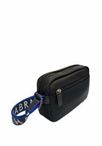 Bolso cruzado negro de nailon con forma rectangular, que cuenta con un cierre de cremallera, una correa azul con un logo y una textura suave.