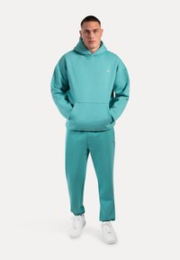Een teal fleece hoodie met een voorzak en bijpassende joggers, met ribgebreide manchetten en witte sneakers. Eenvoudig, ademend materiaal.