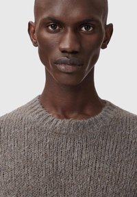 Γκρι πλεκτό πουλόβερ με ραβδωτό στρογγυλό λαιμόκοψη, υφή υφάσματος και διακριτικές αποχρώσεις, που φοριέται από μοντέλο με κοντά κουρεμένα μαλλιά.