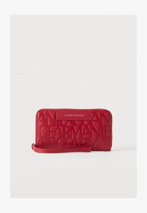 Rødt Armani Exchange armbånds-pung med præget store bogstaver og en aftagelig rem, sat mod en ensfarvet lys baggrund.