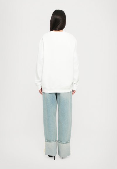 Vit oversized sweatshirt och ljusblå vida jeans med fransade fållar. Enkelt mönster, med en slät textur och avslappnad passform.