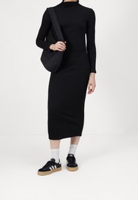 Abito midi nero a coste con maniche lunghe, abbinato a scarpe da ginnastica nere con strisce bianche e calzini grigio chiaro. Borsa a spalla nera imbottita.