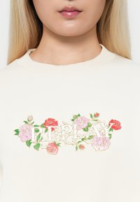 Felpa off-white con ricami floreali in rosa, rosso e verde attorno alla parola "REPLAY", con collo a girocollo a coste.