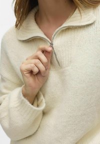 Kremasti zip-up džemper s visokim ovratnikom, od mekanog, teksturiranog materijala s rebrastim rubovima. Ovaj komad ima srebrni zatvarač.