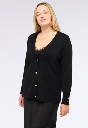 Zwarte cardigan met een V-hals, voorzien van gouden knopen en geribbelde details langs de randen. Draagt over een zwart kanten top.