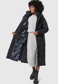 Long black puffer coat with a hood, featuring a vibrant floral patterned lining, zip closure, and red accents. Thick and insulated.