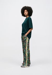 Πράσι νο βαμβακερό μπλουζάκι με κοντά μανίκια, σε συνδυασμό με παντελόνι με λουλουδάτο μοτίβο και κίτρινες ρίγες, καθώς και γκρι και λευκά αθλητικά παπούτσια.