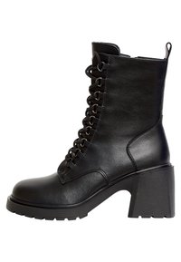 Bottine noire à talon, fabriquée en cuir synthétique, avec un laçage à l'avant, un bout rond et un talon carré texturé.