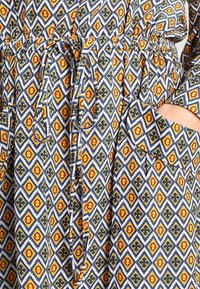 Kolorowa sukienka w wzór diamentów w niebieskim, żółtym i pomarańczowym kolorze. Posiada elastyczny pas i kieszenie boczne.