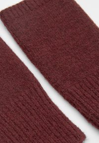 Bordový pletený materiál, měkká textura, žebrovaný vzor, dva překrývající se kusy s mírně chlupatým povrchem a nedokončenými okraji.