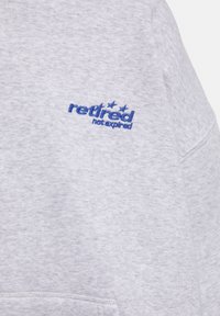 Lichtgrijze trui gemaakt van zachte stof. Voorzien van blauw geborduurde tekst "gepensioneerd, niet verlopen" met drie sterren erboven.