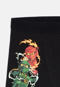 Tissu noir avec un imprimé vibrant représentant deux personnages ninja en rouge et en vert, entourés de flammes et d'effets électriques.