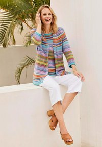 Kleurrijke gestreepte cardigan, blauwe top, witte cropped broek en bruine plateausandalen. Veel strepen in verschillende kleuren; lichte brei-stof.