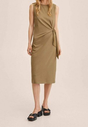 Bezramienna sukienka midi w kolorze oliwkowej zieleni z detalem węzła po boku, noszona z czarnymi sandałami na grubym obcasie z ozdobnymi klamrami.