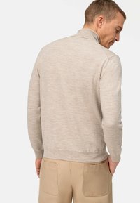 Hellbeiger Pullover mit hohem Kragen, gerippten Bündchen und Saum. Weiche Textur, figurbetontes Design und minimale Details.