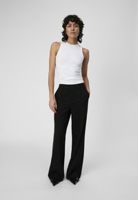 Top sans manches blanc à côtes avec un col rond, associé à un pantalon large taille haute noir et des escarpins noirs à bout pointu.