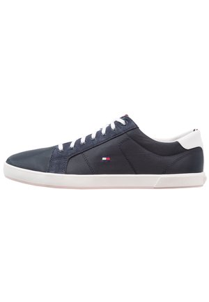 Low-top mørkeblå sneaker med hvide snørebånd og sål, hvid hældetalje og et lille rødt, hvidt og blåt flaglogo på siden.