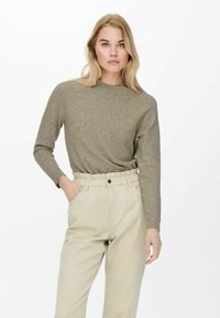 Maglione a maglia verde oliva con scollatura a girocollo e polsini a coste, abbinato a pantaloni beigi a vita alta con cintura elastica.
