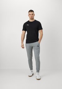 Zwart T-shirt met korte mouwen en wit logo, gecombineerd met lichtgrijze joggingsbroek met bijpassend logo en witte sneakers met bruine zolen.