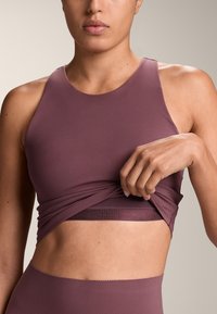 Mauve športni top iz gladkega, raztegljivega materiala. Ima obliko z racerback dizajnom in prilegajoč silhueto, z večplastnim detajlom na dnu.
