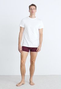T-shirt en coton blanc associé à un boxer bordeaux. La tenue présente un design simple, des manches courtes et un col rond.