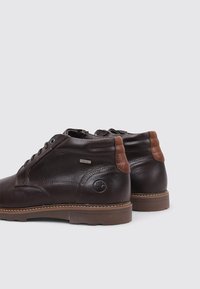 Botas de tobillo de cuero marrón con acentos de cuero marrón claro, punta redonda, diseño de cordones y suela de goma. Presenta un logotipo en el lateral.