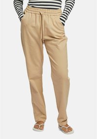 Beiga, lätta, dragsko-byxor med avslappnad passform. Har elastisk midja och sidofickor. Kombineras med vita sandaler.