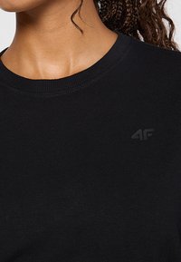 Czarna bawełniana koszulka z okrągłym dekoltem i prążkowaną fakturą. Posiada małe, wytłoczone logo na lewej stronie klatki piersiowej.