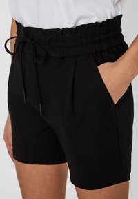 Shorts noirs avec une ceinture élastique et un cordon de serrage ajustable, dotés de poches latérales et d'une texture de tissu lisse.
