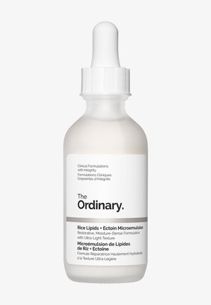 Botella cuentagotas con acabado blanco opaco, banda plateada y tapa blanca. Presenta una etiqueta con texto que detalla los ingredientes y detalles del producto.