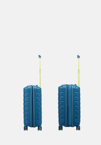 Valigia rigida blu con finitura testurizzata, manico telescopico giallo e due ruote, dotata di chiusura centrale con cerniera.
