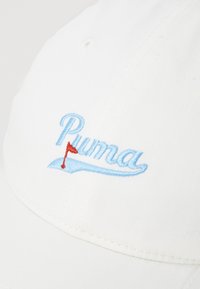 Cappello bianco in cotone con il testo "Puma" ricamato di colore azzurro chiaro e un piccolo design di bandiera rossa sulla parte anteriore. Texture liscia, forma classica.