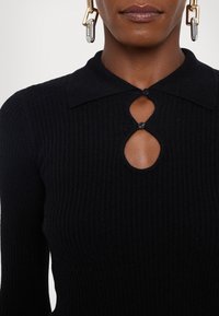 Μαύρο πλεκτό τοπ με ραβδώσεις, χαρακτηριστικά στρογγυλή λαιμόκοψη, άνοιγμα σε σχήμα κλειδώματος με κουμπί και μακριά μανίκια. Λείο υφή.