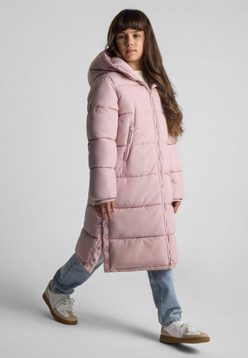 Lång rosa vadderad kappa med huva, med sydda paneler, dragkedjestängning och sidoknappar, matchad med denim och avslappnade sneakers.