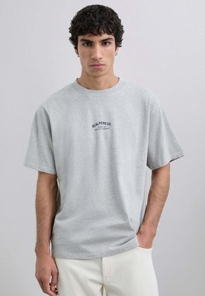 Camiseta de algodón gris con mangas cortas, escote redondo y bordado en azul marino "SCALPERS CO" en el pecho. Diseño simple y de corte relajado.