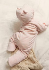 Baby onesie van zachtroze stof, met een berenkap met oren, bloemachtige textuur, en een comfortabele pasvorm, liggend op een beige gebreide deken.