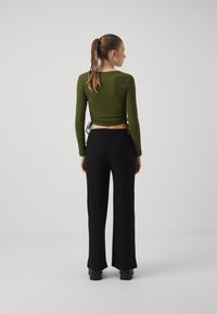 Olive green ribbed long-sleeve top with side ties paired with black, wide-leg ribbed pants. The outfit features a fitted and structured design.