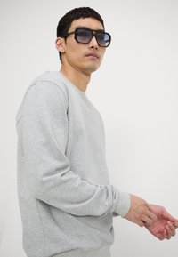 Gray sweatshirt with long sleeves, round neck, and ribbed cuffs. Dark sunglasses with a bold geometric frame, featuring a tortoiseshell pattern.