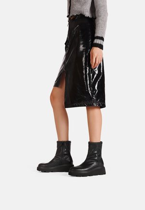 Gonna in finta pelle lucida nera con uno spacco laterale, abbinata a stivali in pelle nera fino alla caviglia con suola spessa e chiusura con zip.