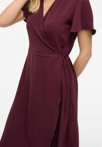 Vestido envolvente burdeos en tejido texturizado, con mangas cortas, escote en V y un detalle atado en la cintura, que cae hasta la mitad de la pantorrilla.