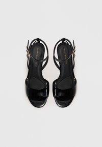 Svarte lakkledder åpne tå sandaler med ankelremmer og gullfargede spenner, flat såle, og Tommy Hilfiger merkevare inne.